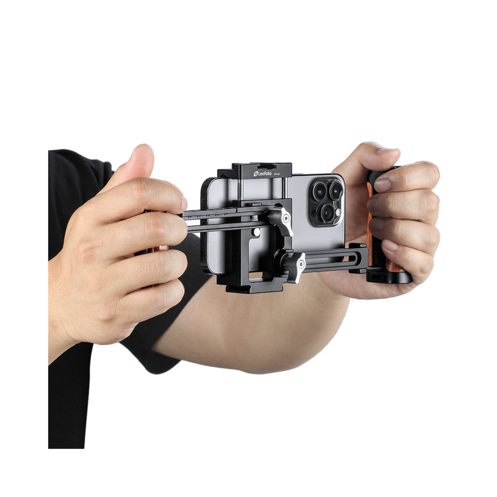 Hands holding a Leofoto PH-01 smartphone cage rig with articulated arms and stabilizer handles, demonstrating in-use operation from a front view.