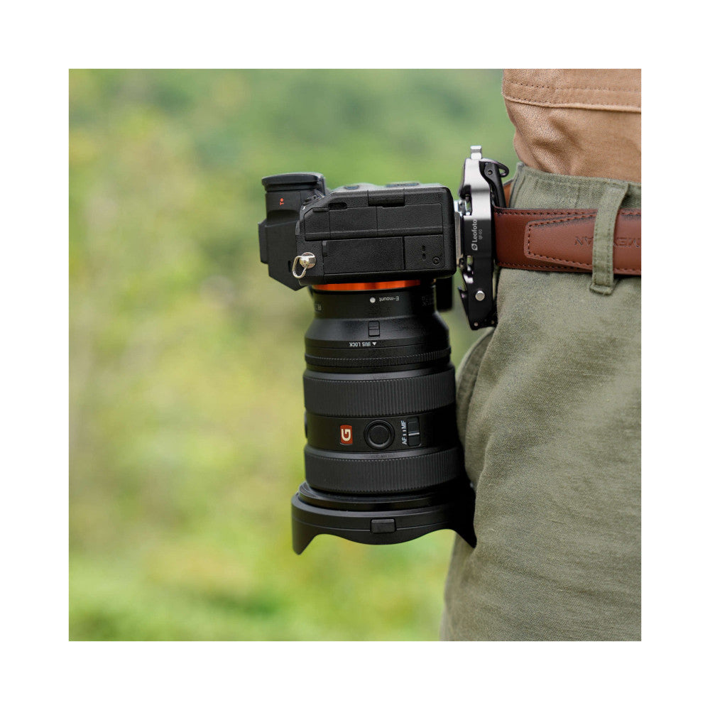 Leofoto QF-03 quick release mount attached to camera lens on person wearing brown belt and green shirt, showing side angle view in outdoor setting.