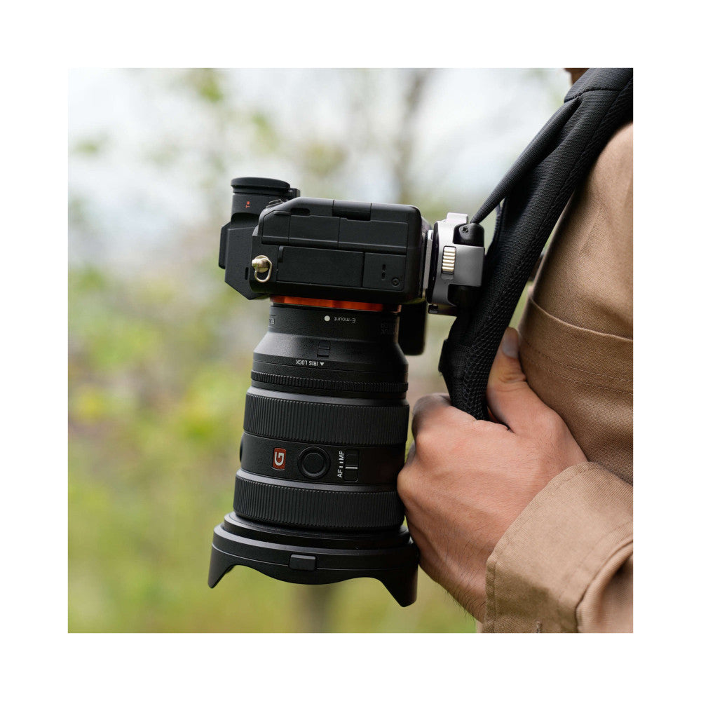 Camera lens with silver quick-release mount attached, held in hands outdoors with blurred green background.