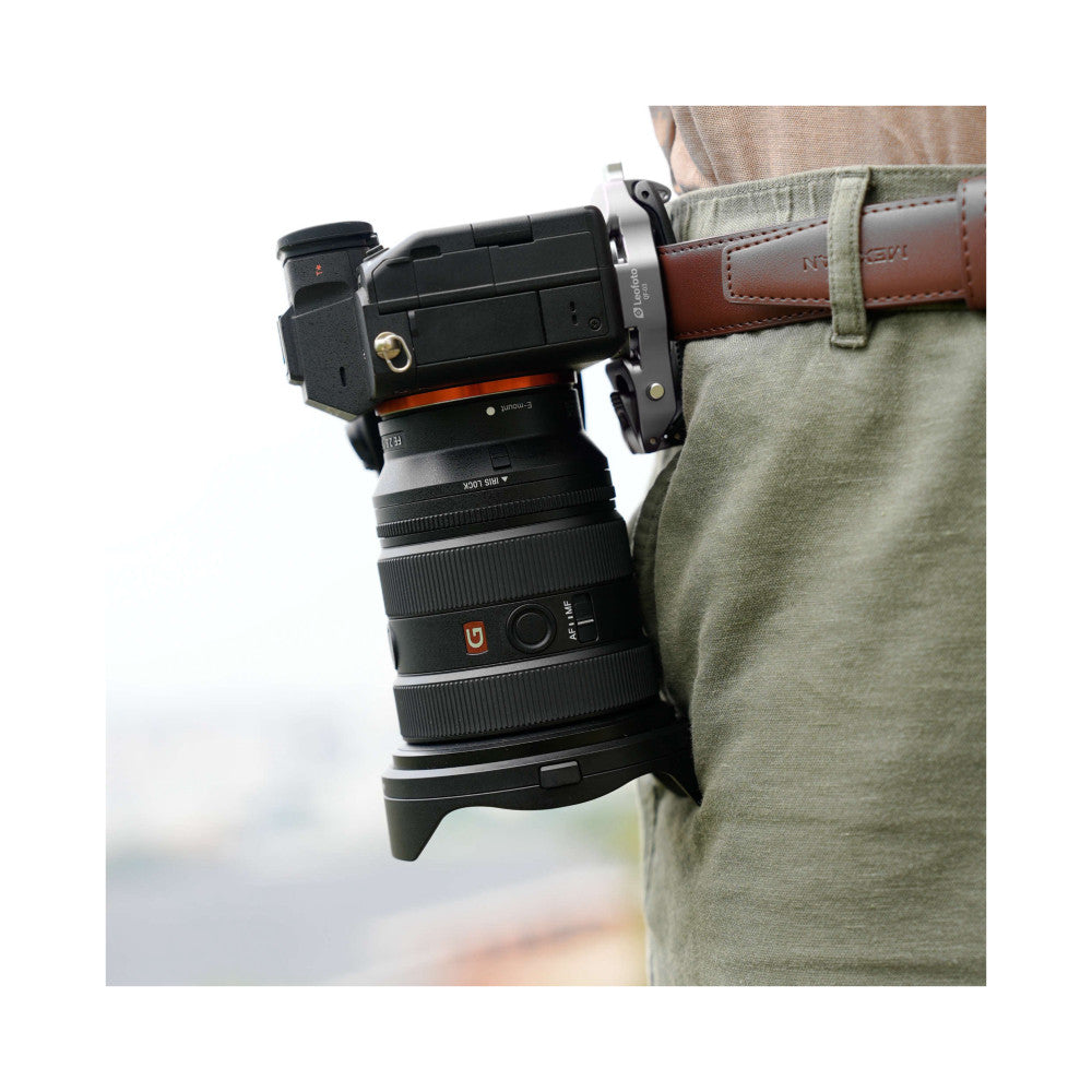 Camera mounted on khaki canvas bag strap using silver quick-release mount, shown in-use from side angle.