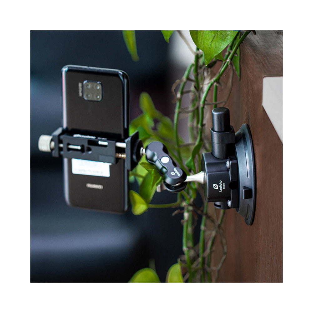 Smartphone mounted on suction cup with articulating arm attached to wooden surface, surrounded by green foliage, demonstrating in-use setup.