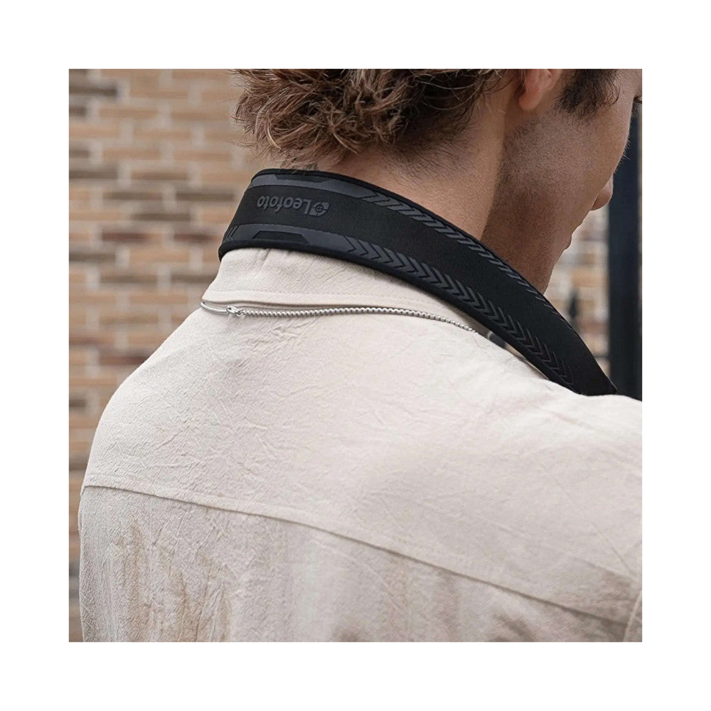 Man wearing black camera strap across shoulder over light beige shirt, rear view against brick wall background