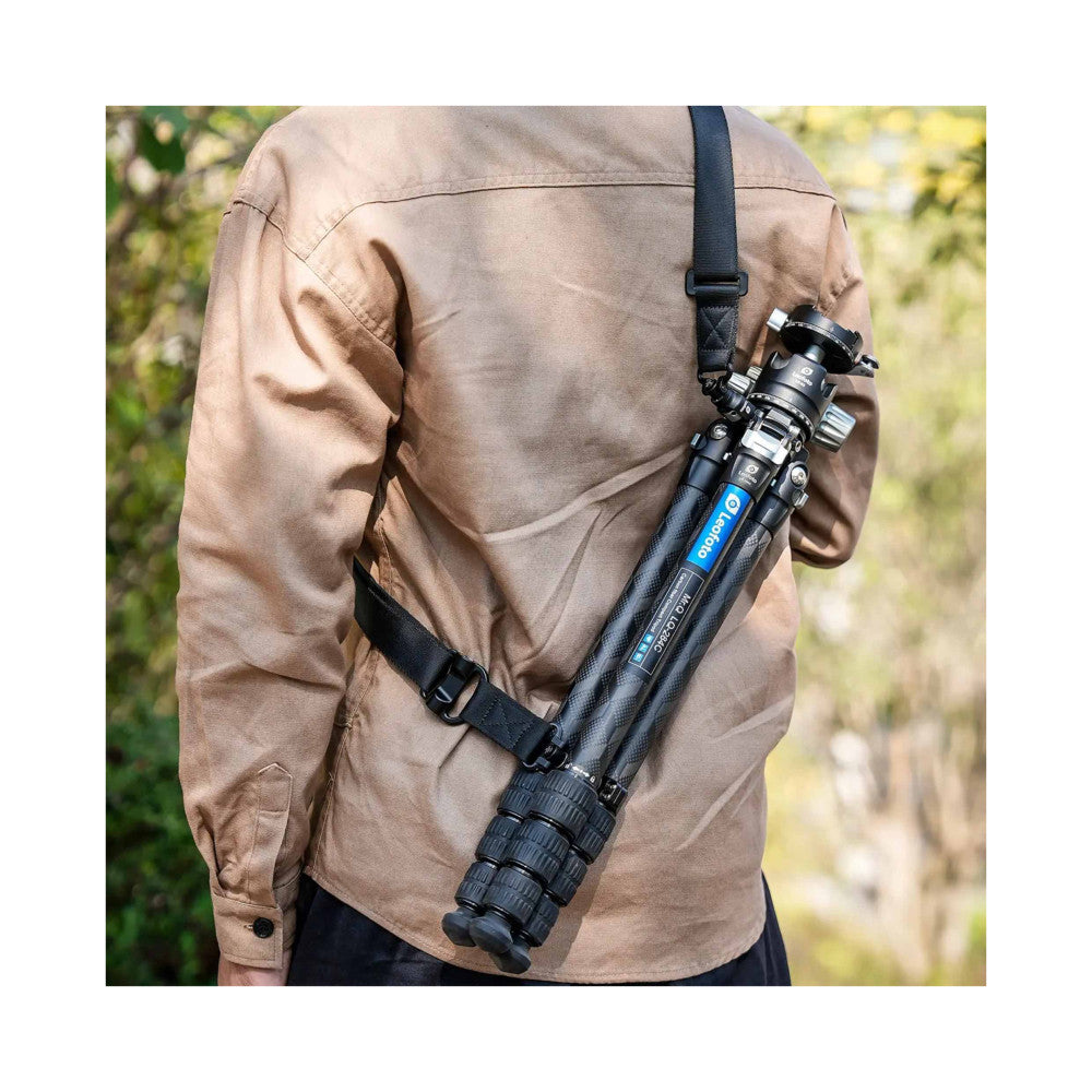 Person wearing beige jacket with black camera strap attached to video camera mounted across their back, demonstrating in-use positioning outdoors.