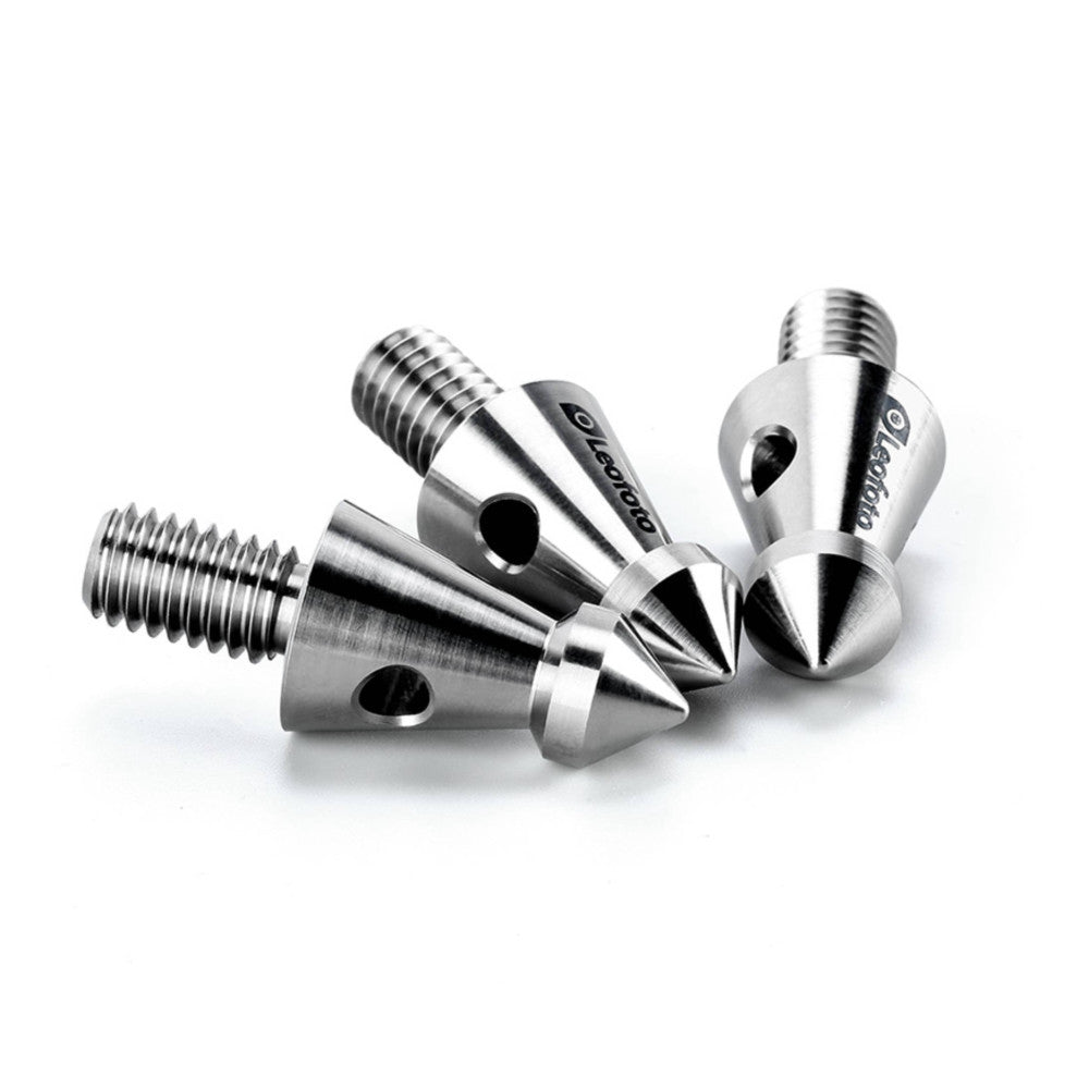 Four titanium tripod spikes with threaded tops arranged in a group against white background, showing pointed cone tips and central mounting holes from a close-up angled view.
