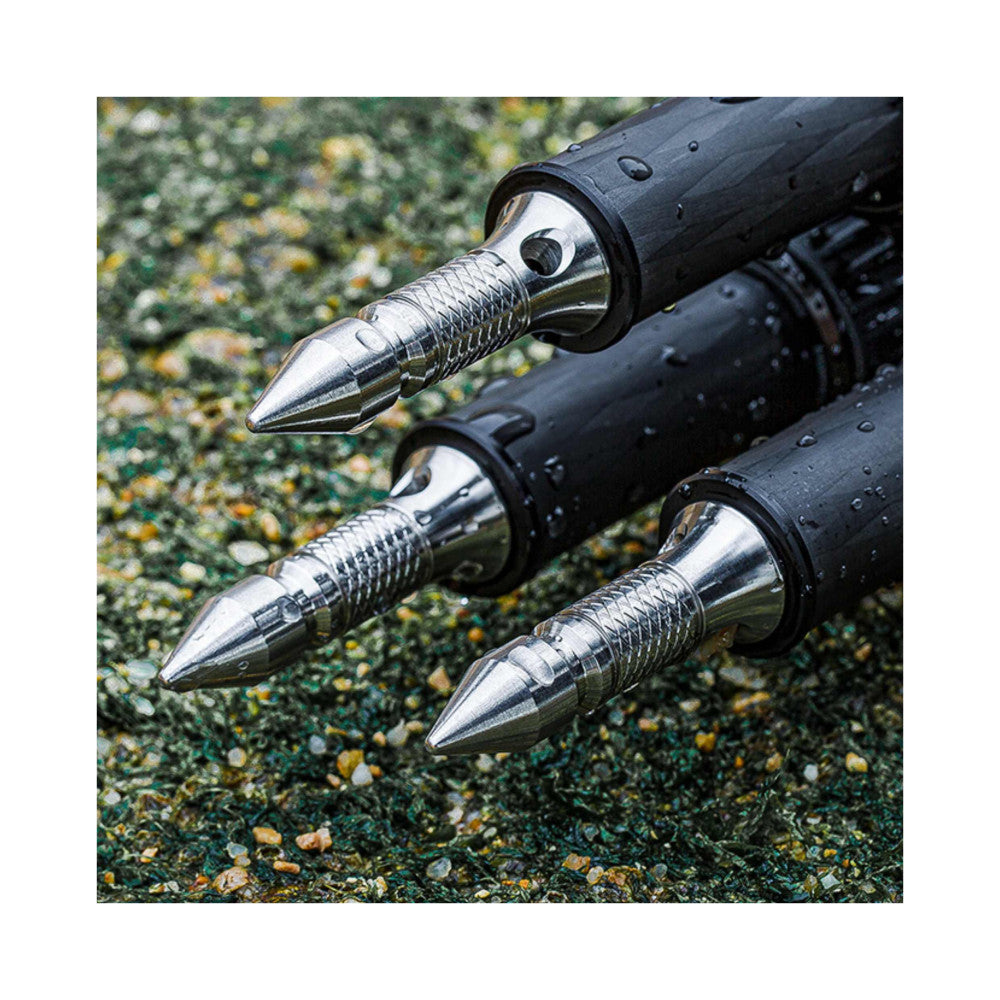 Close-up detail of three polished stainless steel tripod spikes with textured grip sections and black rubber sleeves, arranged diagonally on a textured green surface.