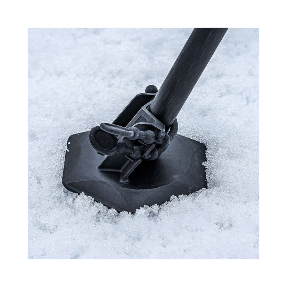 Black tripod snow shoe attachment on ice surface, angled side view showing curved base and mounting mechanism with wooden pole.