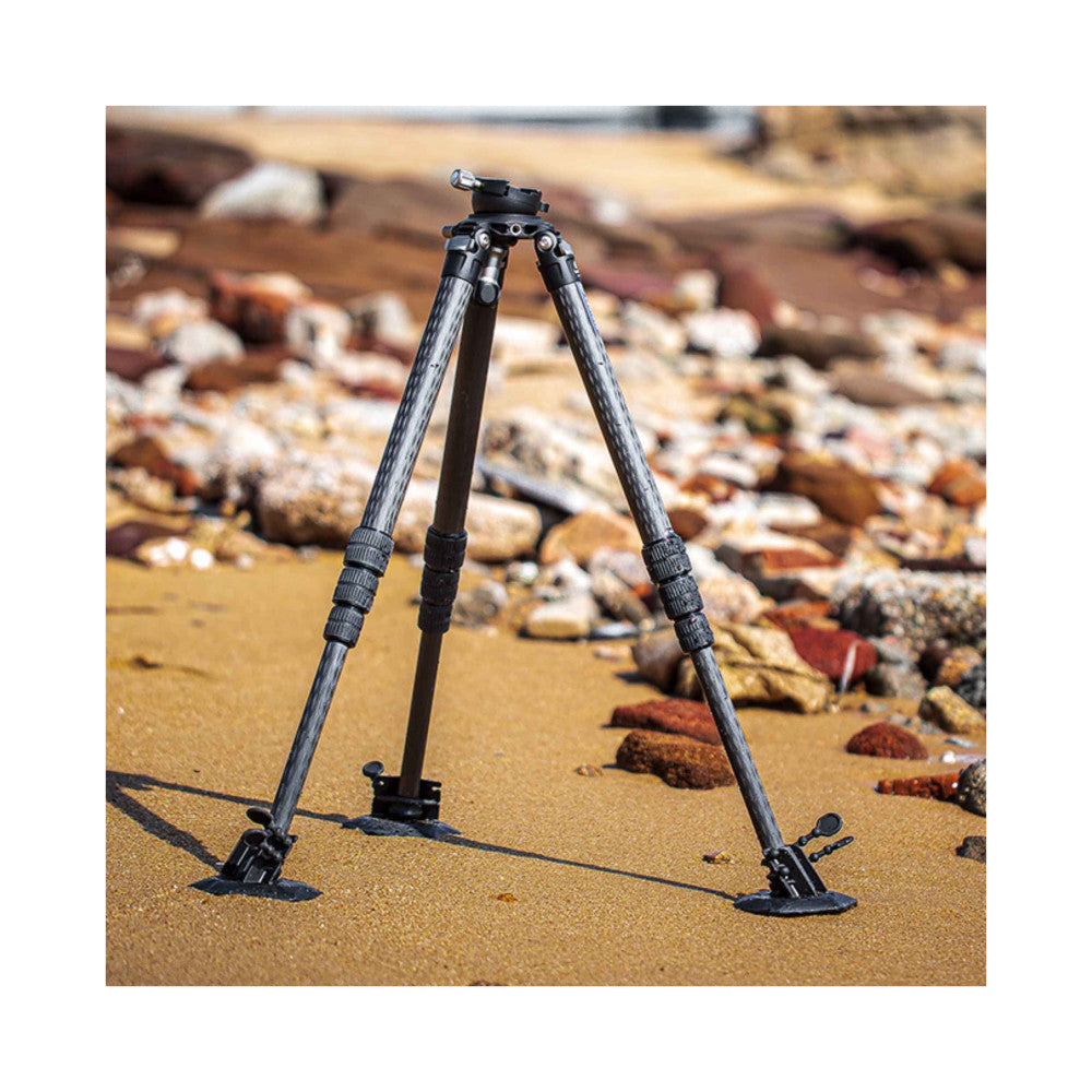 Leofoto tripod with snow/sand shoes deployed on a beach, showing the wide base feet and leg extensions from a front angle.