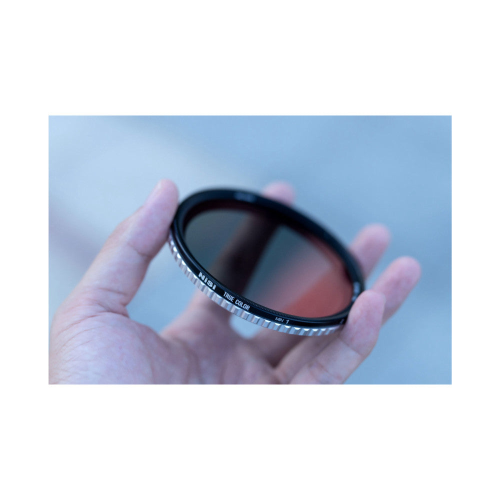 Close-up of a NiSi circular filter held in someone's hand against a blue sky background, showing the filter's dark glass and labeled ring.