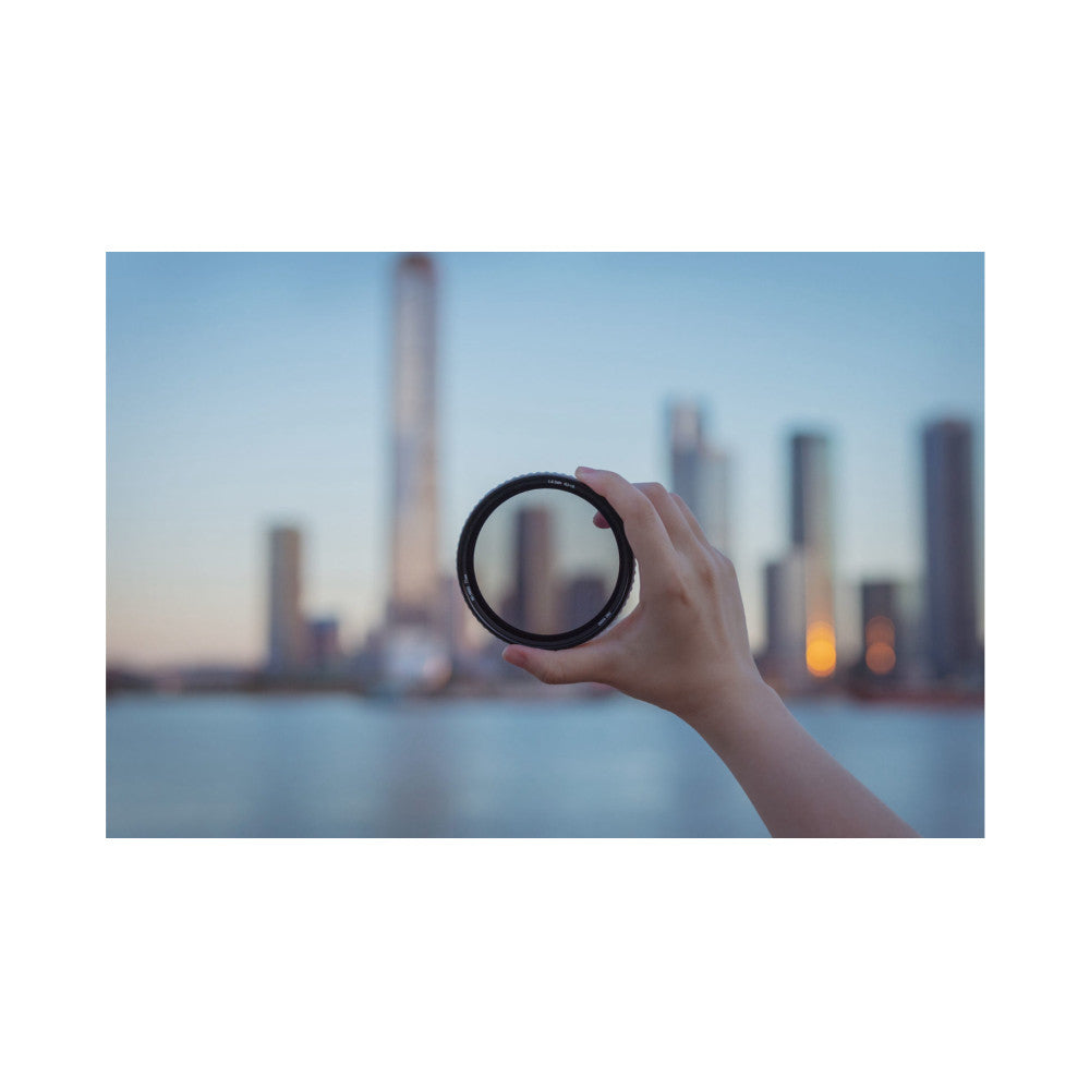 Hand holding a circular filter ring against a blurred cityscape skyline at dusk, demonstrating in-use application.