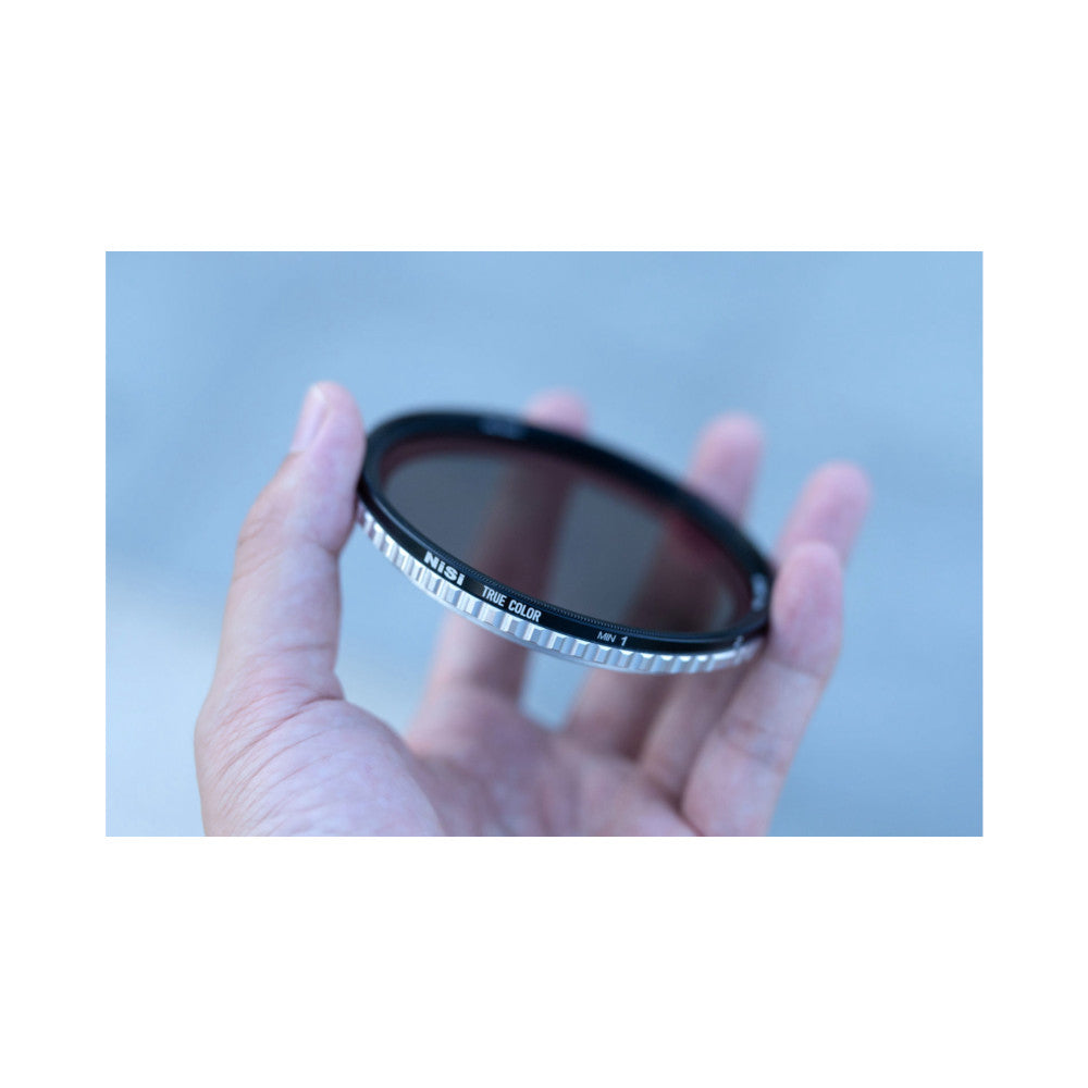 Hand holding a circular NiSi camera filter against blue sky, showing the filter's dark glass and labeled metal ring.