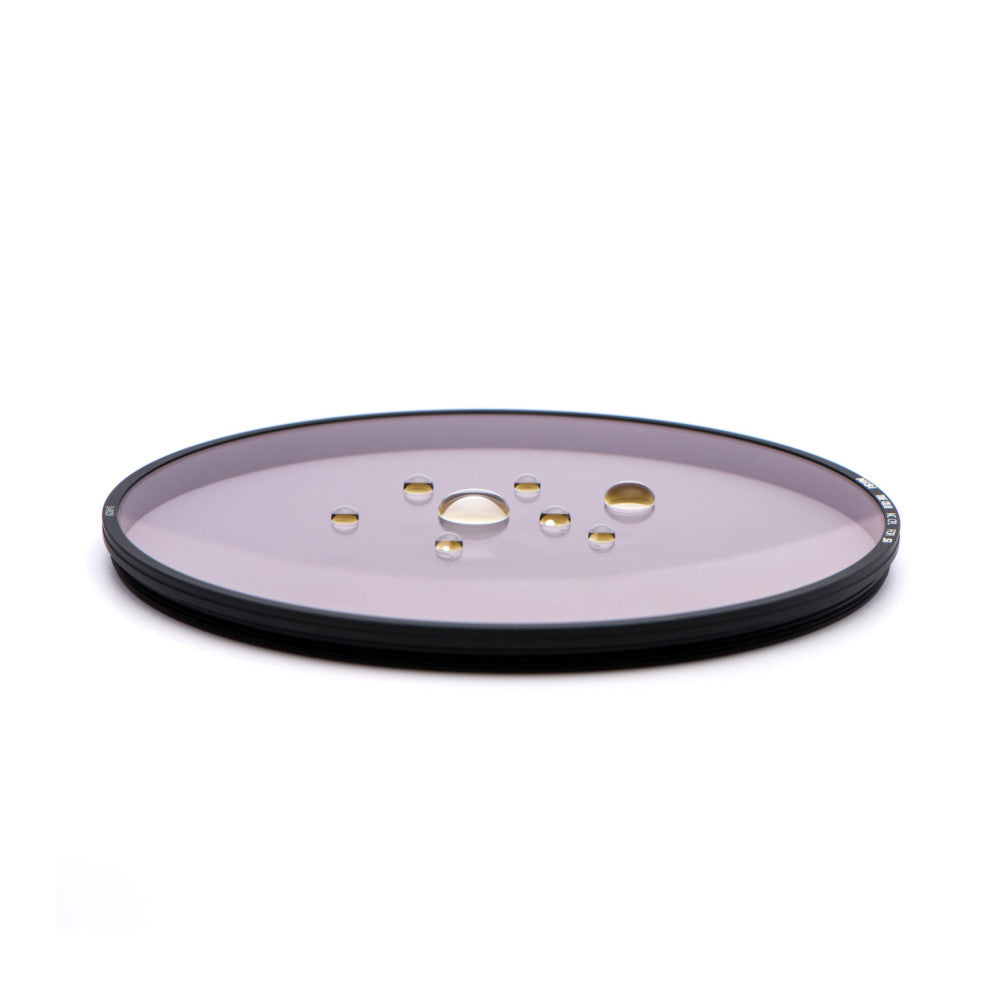 Overhead view of a round filter holder with a pink-tinted glass surface and black rim, displaying water droplets.