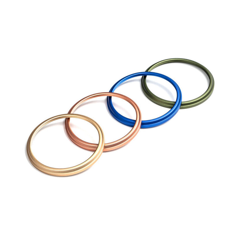 Four overlapping decorative camera rings in gold, rose gold, blue, and green arranged diagonally on white background.