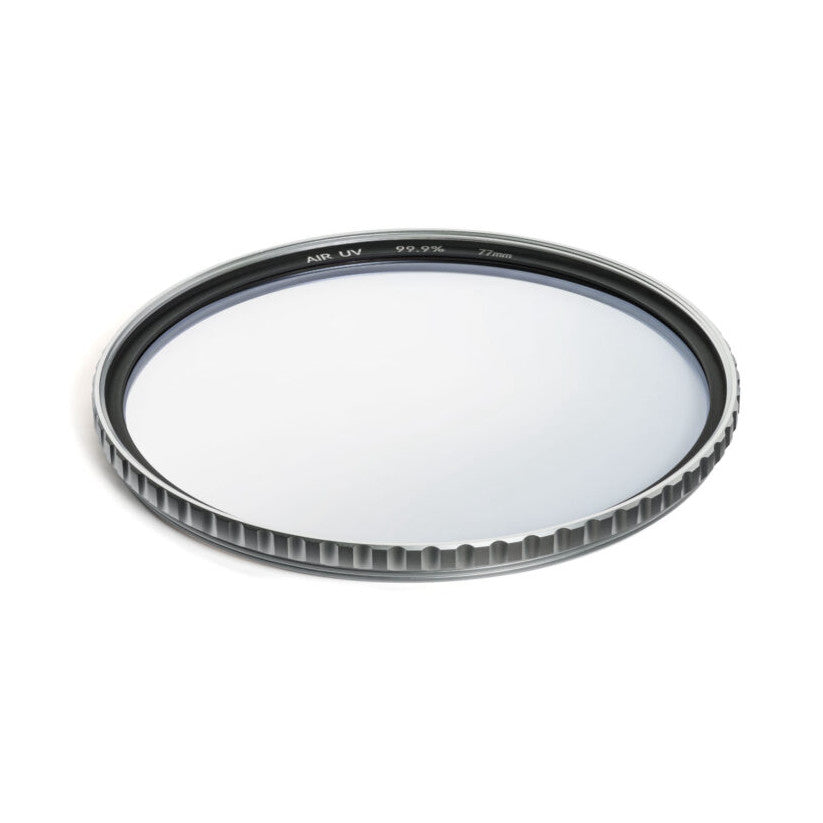 Overhead angled view of a circular camera filter with black rim and ribbed metal edge, showing the clear glass surface and product markings on the frame.
