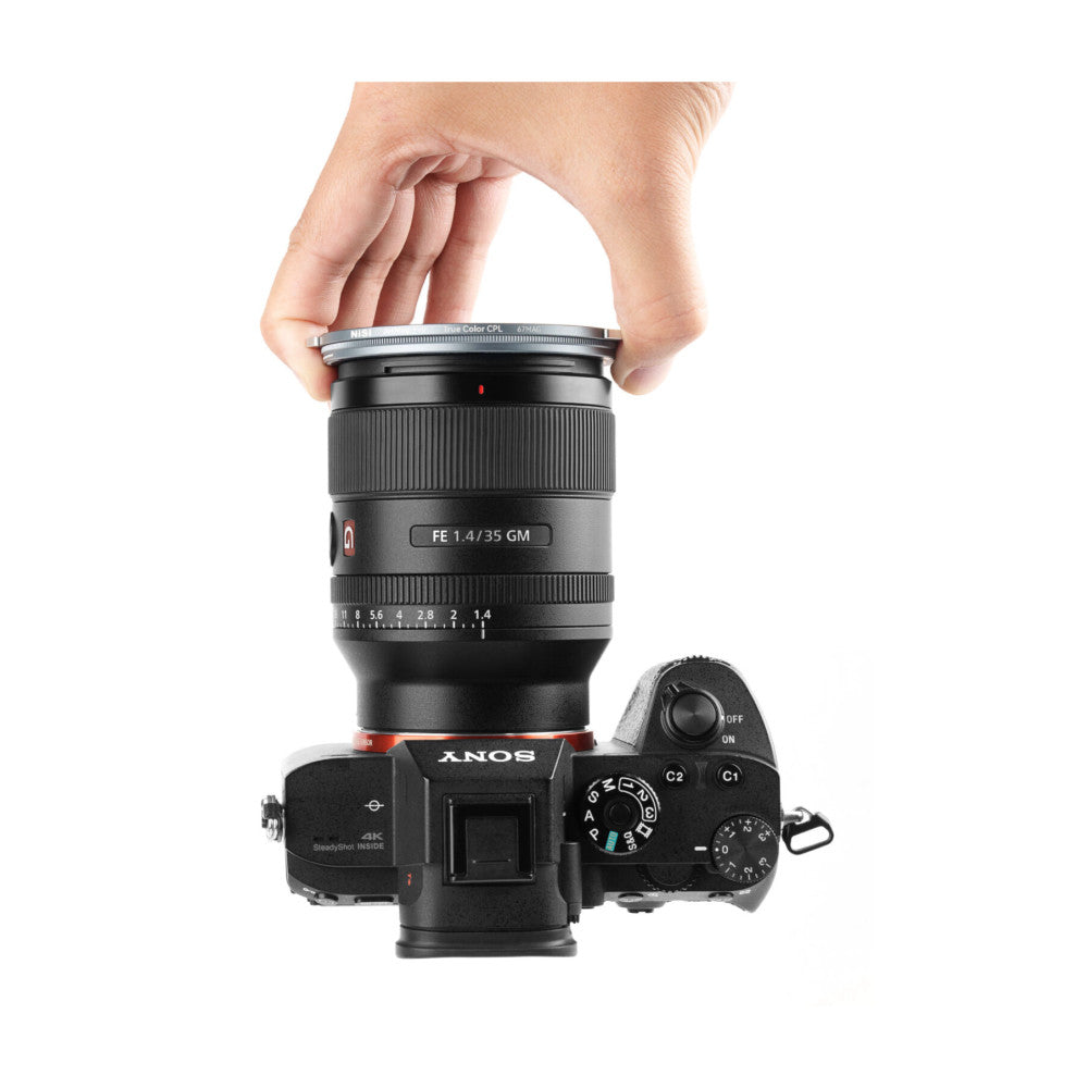 Hand removing a circular filter from the top of a Sony mirrorless camera with attached 35mm lens shown from above.
