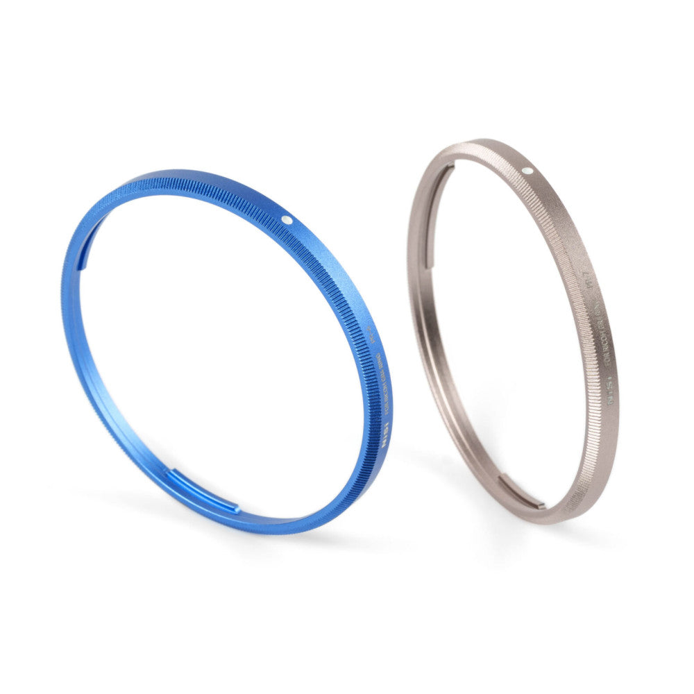 Two lens cap rings displayed side by side - one blue and one titanium gray, shown at an angle against a white background.