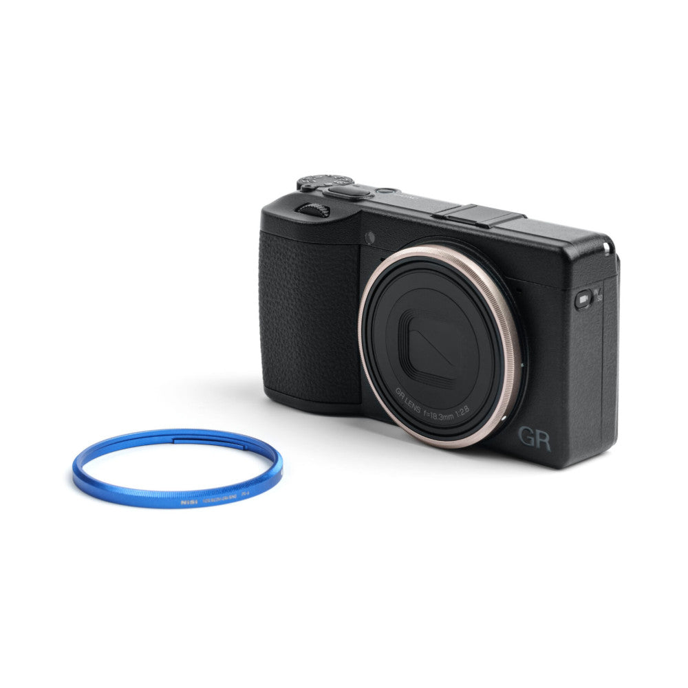 Black Ricoh GR compact camera displayed at three-quarter angle with blue ring cap positioned in front on white background.