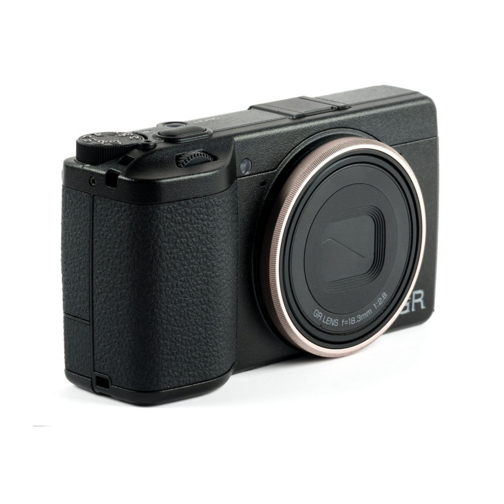 Black compact camera with textured grip, shown from three-quarter angle displaying the lens with silver ring accent.