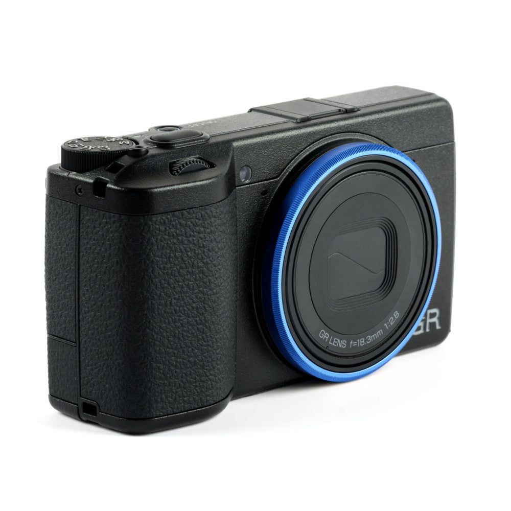 Black compact camera with blue ring around lens, shown at three-quarter angle against white background.