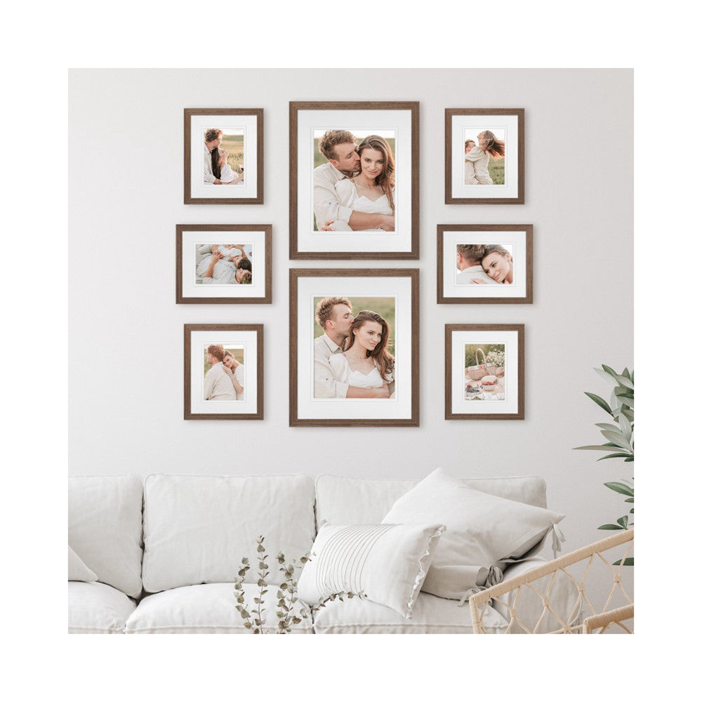 Gallery wall display of eight wooden frames with matting arranged symmetrically above a white sofa in a living room setting.