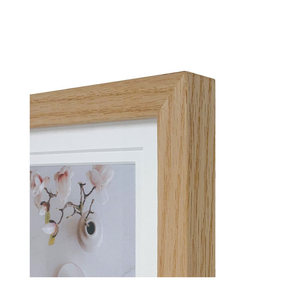 Close-up detail of natural wood frame corner showing grain texture and white matting with framed floral artwork visible inside.