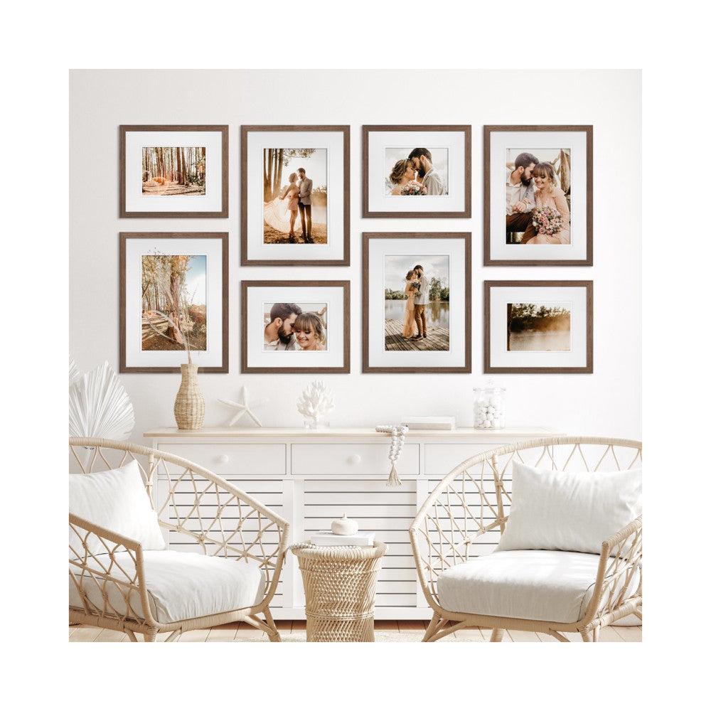 In-use photo showing eight brown wooden frames displaying wedding and couple photos arranged on a white wall above a console table and wicker chairs.