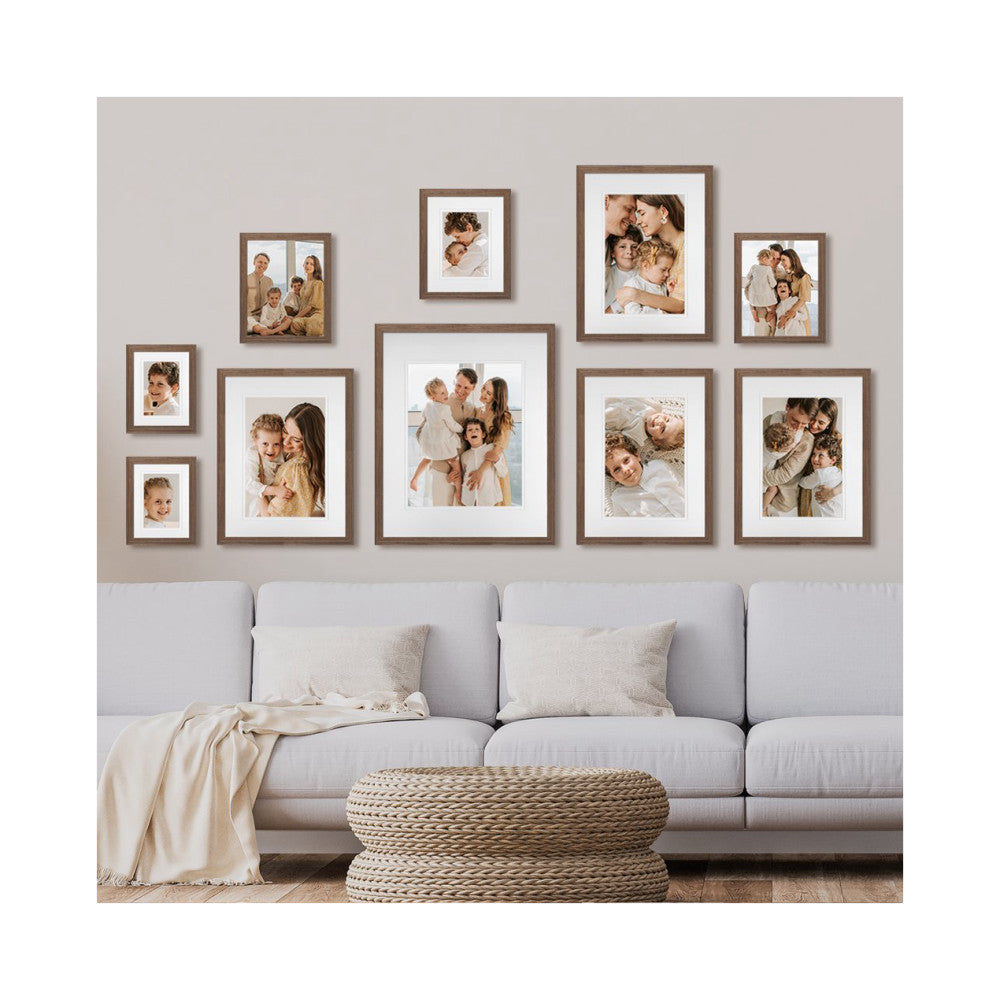 Gallery wall with 10 chestnut frames of varying sizes displaying family photos above a light gray sofa with neutral décor.