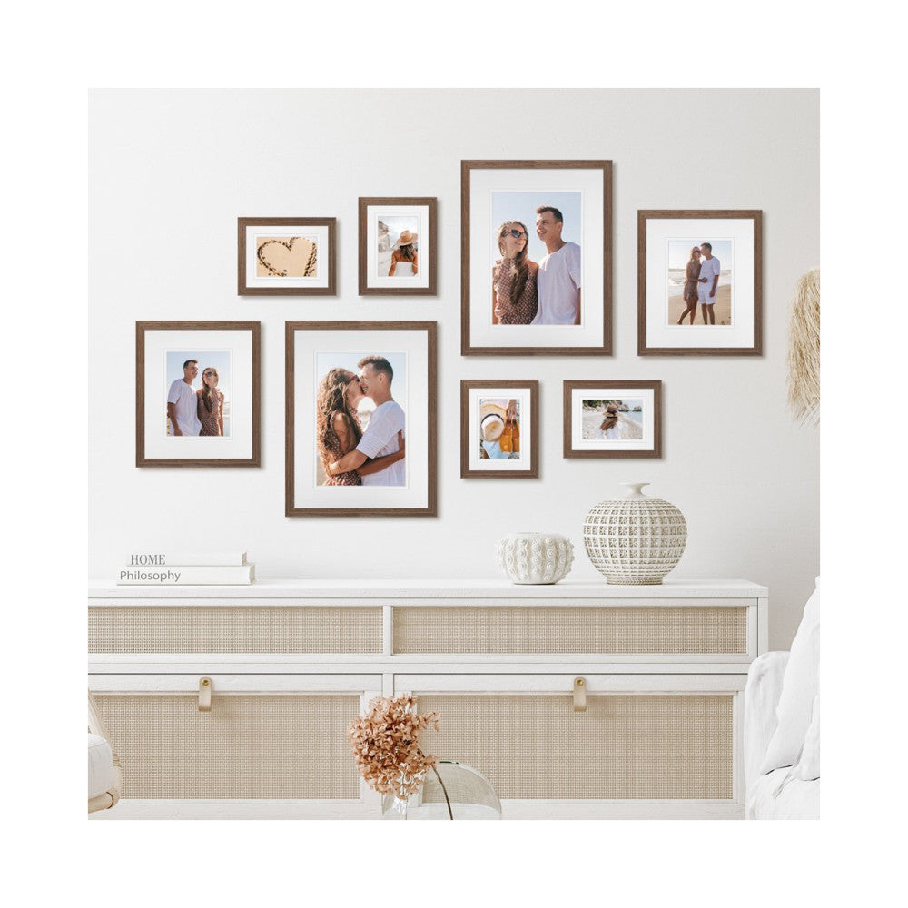 In-use gallery wall display showing eight wooden frames in chestnut finish arranged on a beige wall above a white dresser with decorative items.