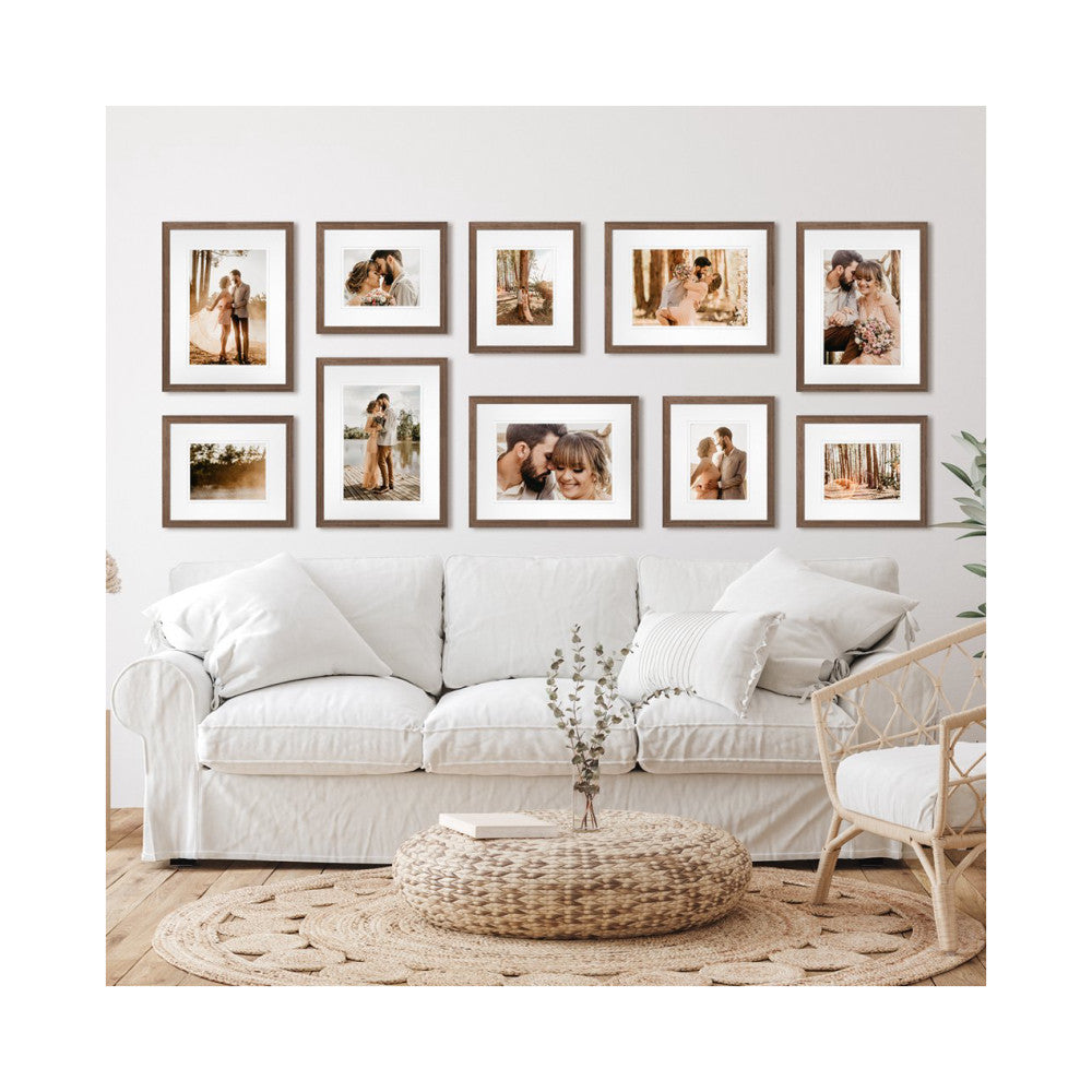 In-use photo showing ten chestnut-framed photos arranged on a living room wall above a white sofa with neutral decor.
