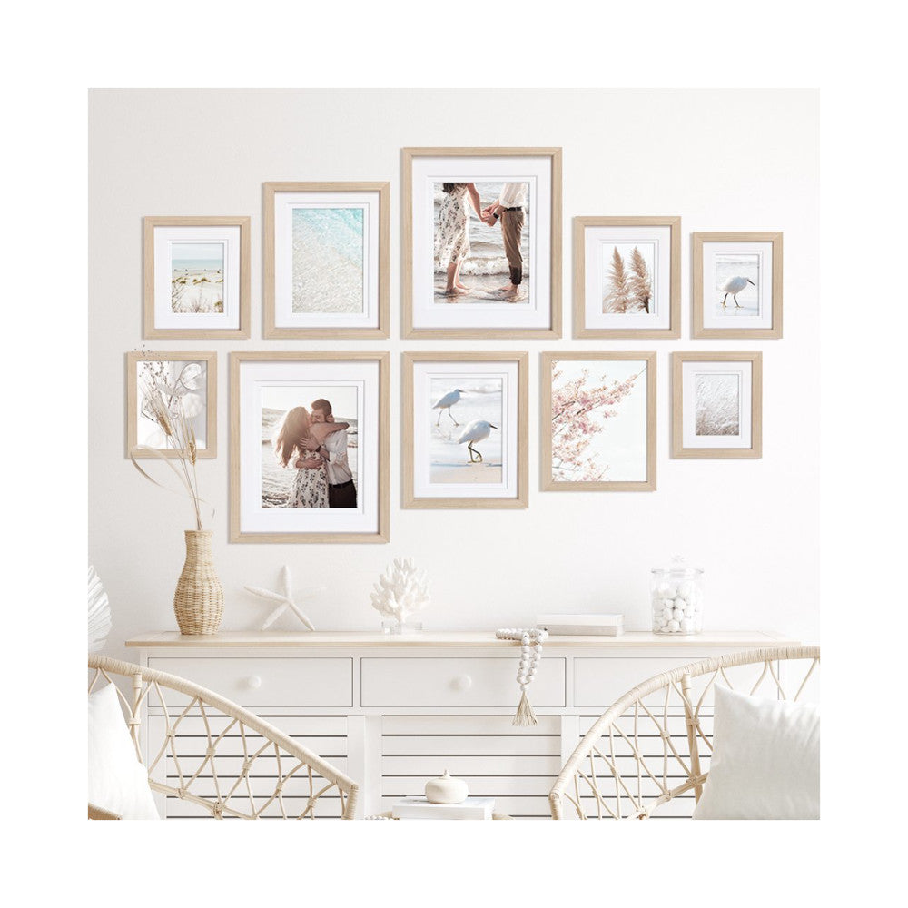 Ten wooden frames arranged on a white wall above a console table, displaying coastal and nature photos in a gallery wall layout.