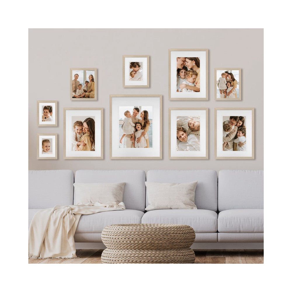 Gallery wall display above a gray sofa showing 10 framed family photos in light wood frames arranged in an asymmetrical pattern.