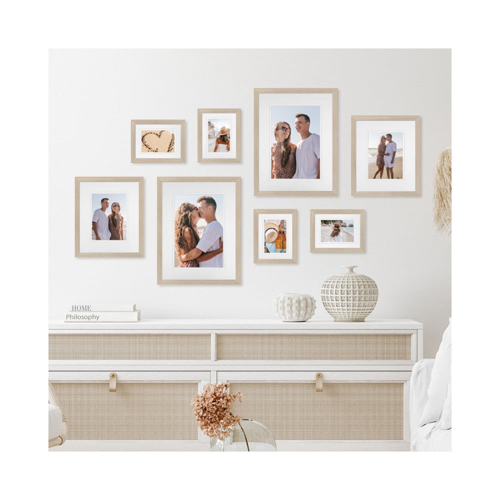In-use photo showing eight natural wood frames arranged on a wall above a white dresser with decorative items and beach-themed family photos.
