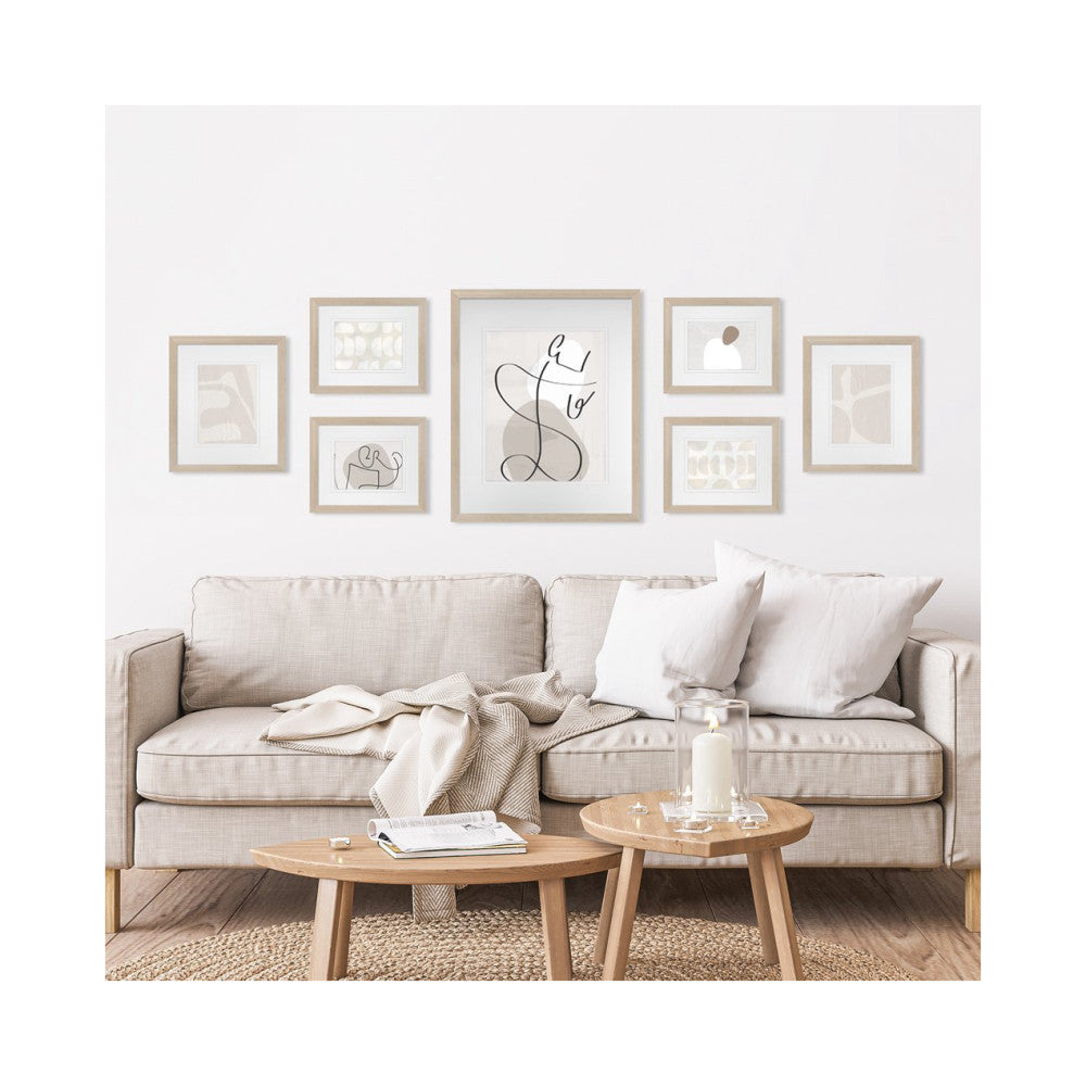 Seven framed artworks arranged above a beige sofa with wooden coffee tables and neutral décor in a living room setting.