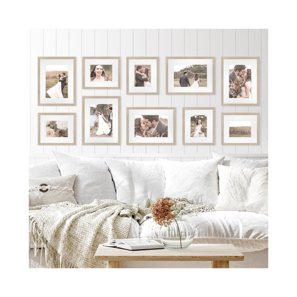 Ten wood-framed wedding photos displayed on a white shiplap wall above a white upholstered sofa with cream bedding and a wooden table.