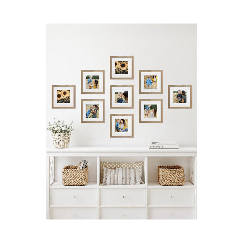 Nine natural oak frames arranged in a gallery wall display above white storage furniture with decorative baskets and plants.