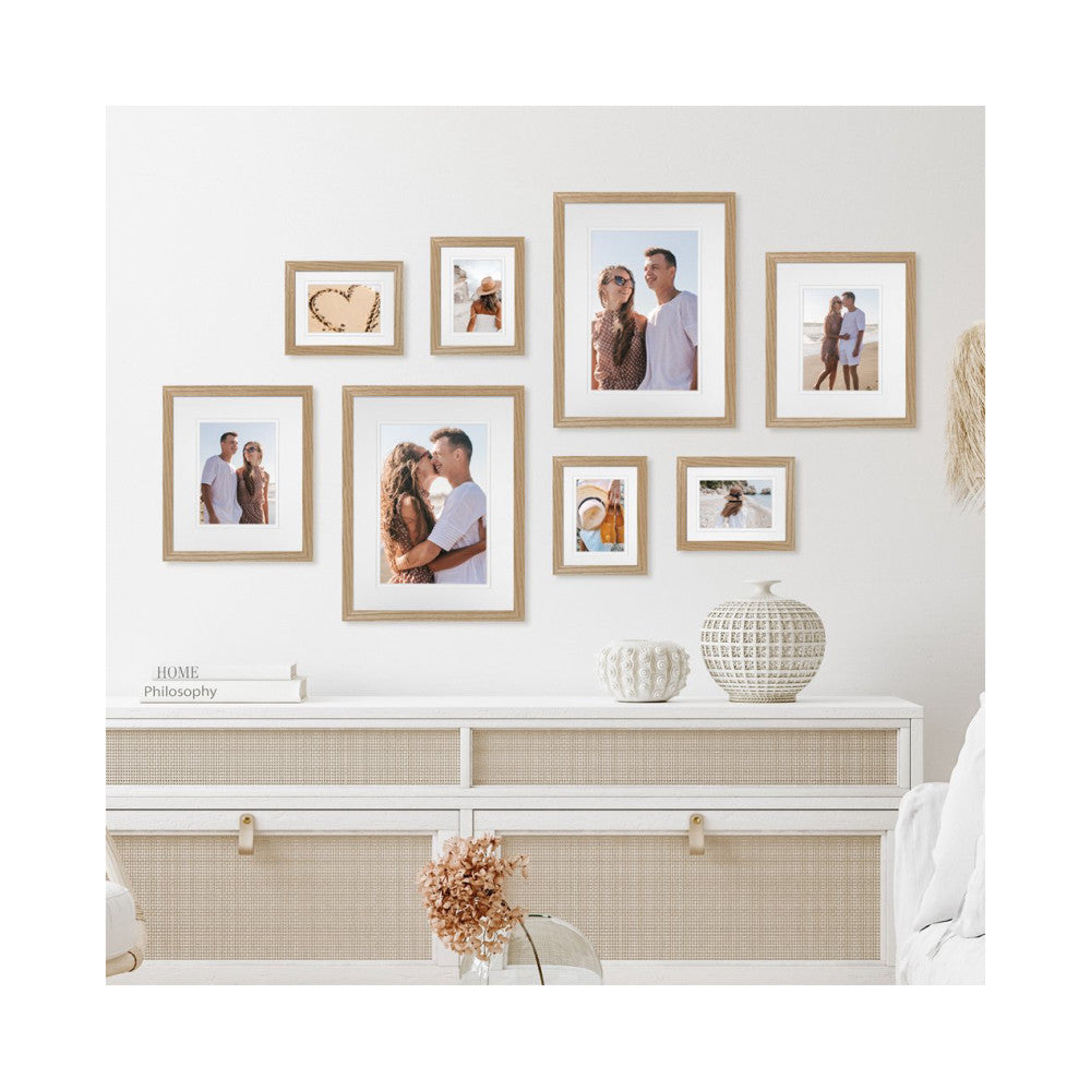 In-use photo showing eight natural oak frames arranged on a white wall displaying beach vacation photos above a white dresser with decorative items.