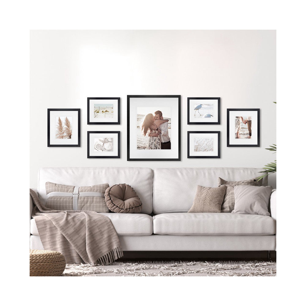 Black framed gallery wall display above a cream sofa, showing seven frames with nature and family photos arranged in a symmetrical pattern.