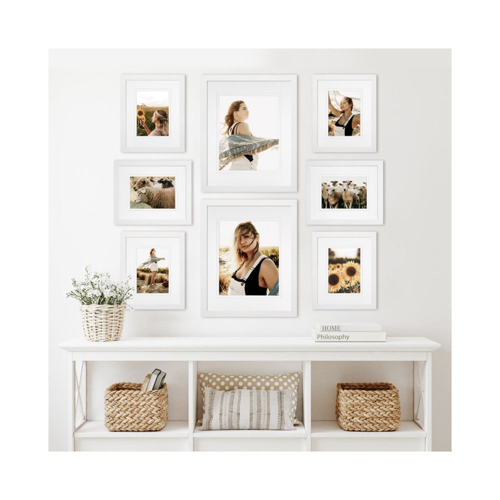 Gallery wall display showing eight white framed photos arranged on a wall above a white storage unit with woven baskets.