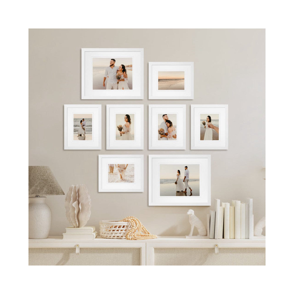 White framed gallery wall display with eight frames hung on beige wall above shelf with decorative items and books.