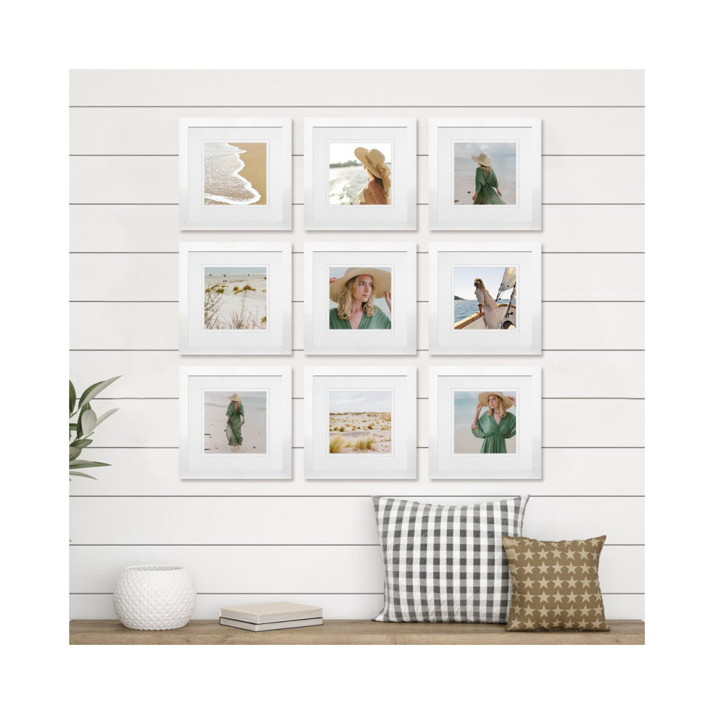 Nine white gallery frames arranged in a 3x3 grid on shiplap wall, displaying beach and portrait photos above a wooden bench with pillows.