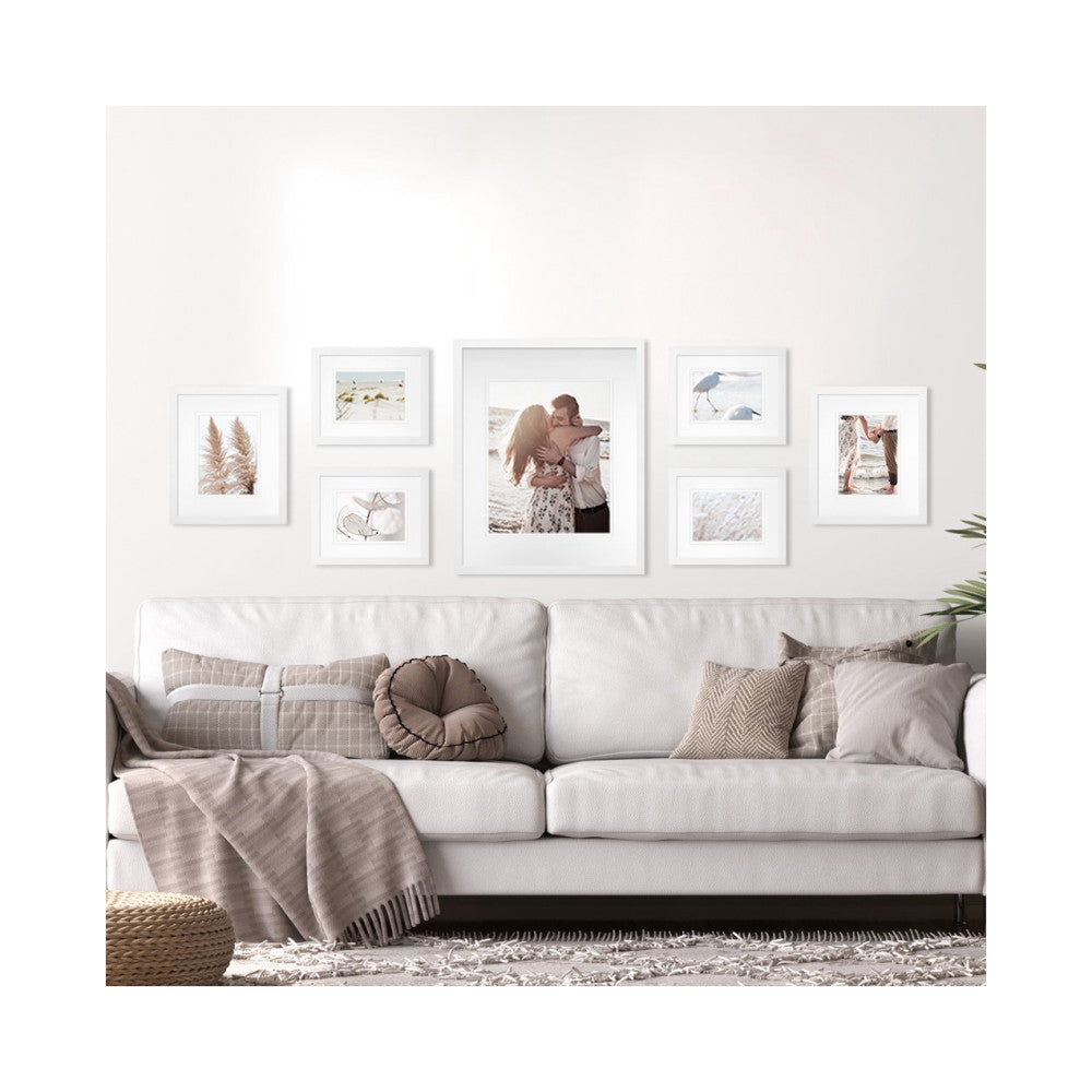 White framed gallery wall arrangement of seven frames displayed above a cream-colored sofa with neutral pillows and throw blanket.