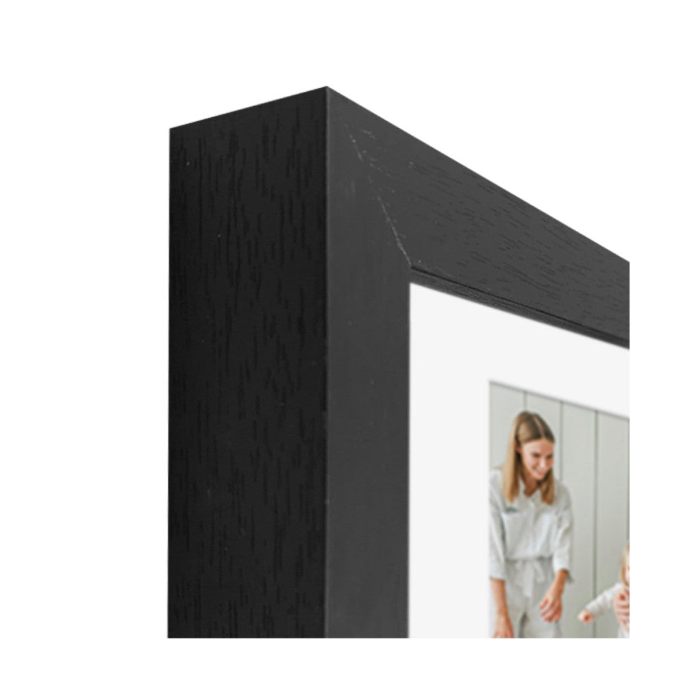 Close-up detail of black wooden frame corner showing wood grain texture and white mat with partial photo visible inside.