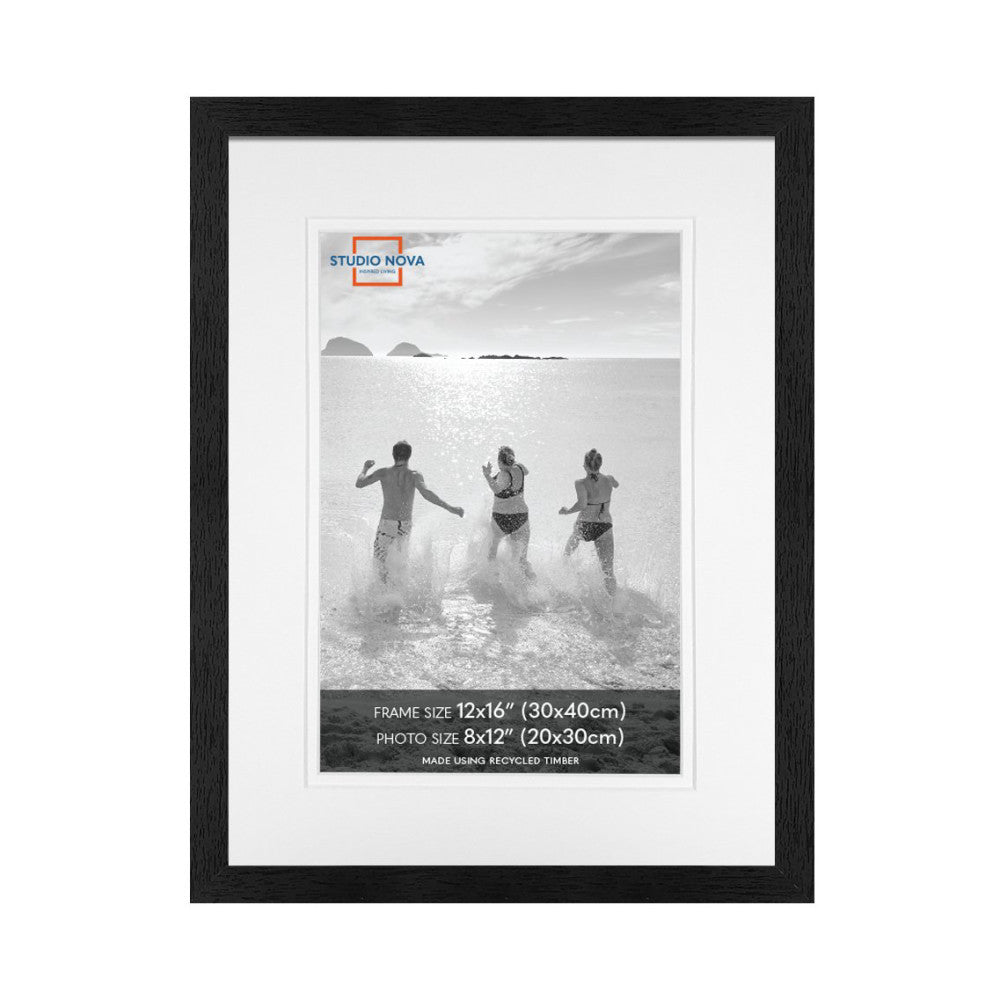 Black wooden picture frame with white mat displaying black and white beach photo of three people running into the ocean.