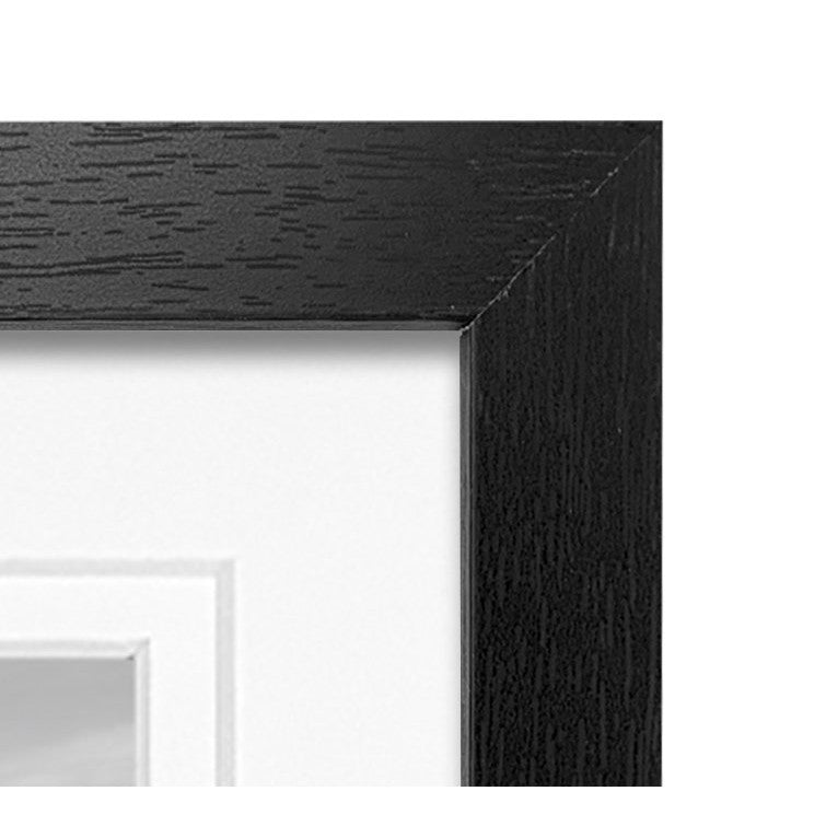 Close-up detail of black wooden frame corner showing wood grain texture and inner mat edge against white background.
