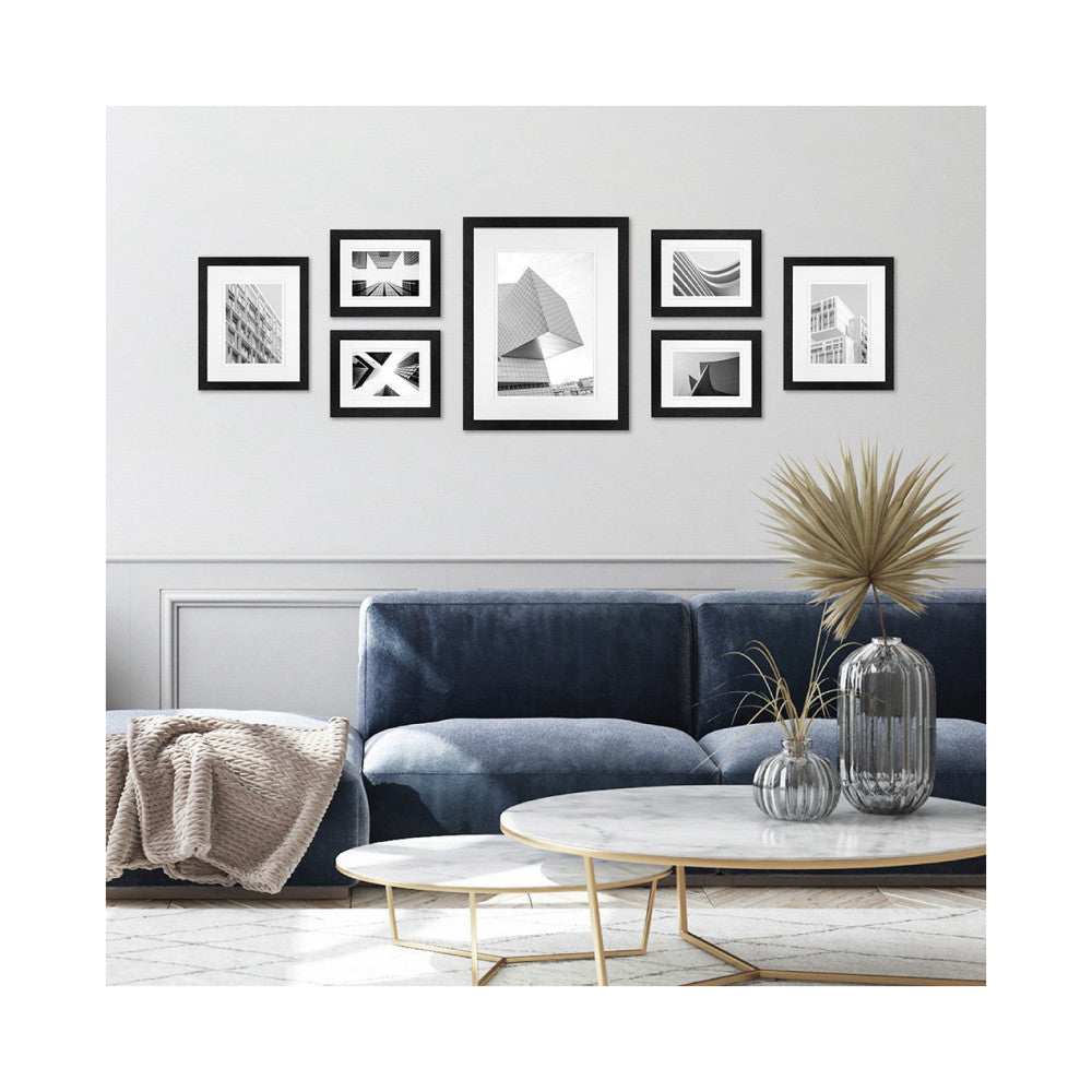 Black framed gallery wall display with seven frames containing black and white architectural photography above a blue sofa.