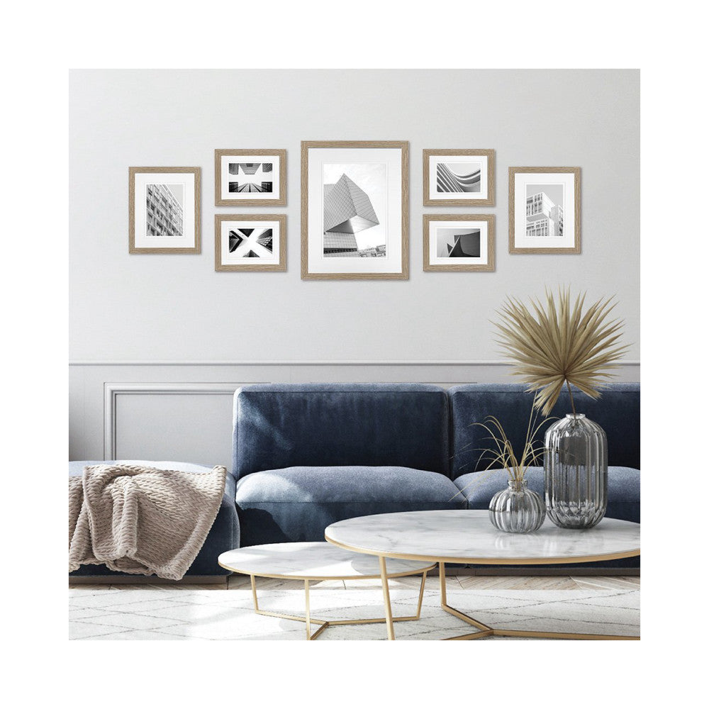 Gallery wall display of seven wooden frames with black and white architectural photos hung above a blue sofa in a modern living room setting.