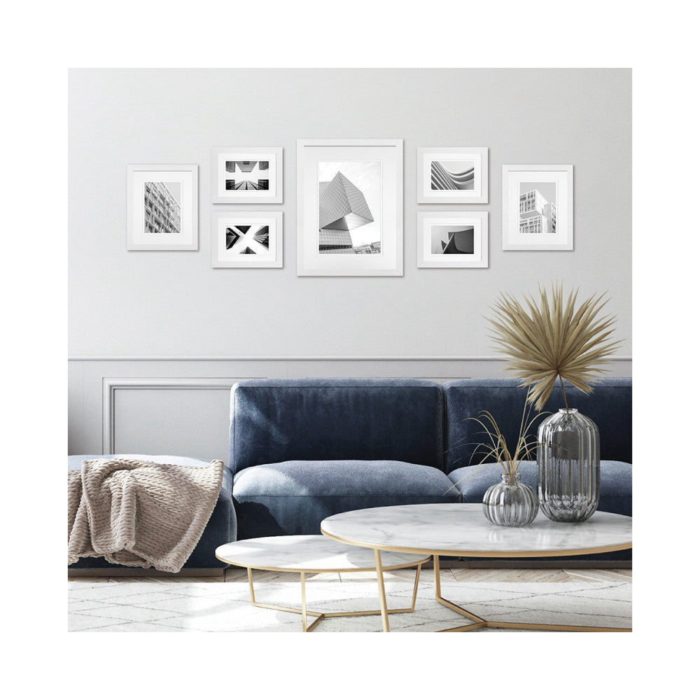 Modern living room with white framed gallery wall displaying black and white architectural photography above a blue sofa and marble tables.