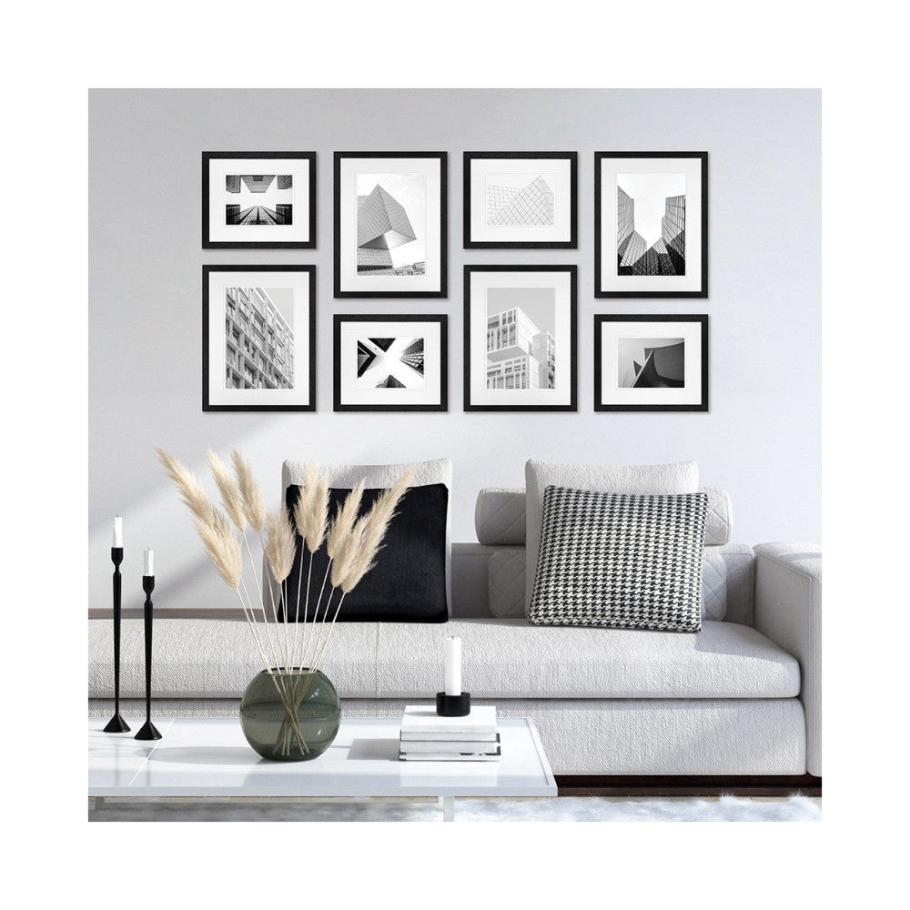 Eight black-framed architectural photographs displayed on a light wall above a gray sofa with decorative pillows and accessories.