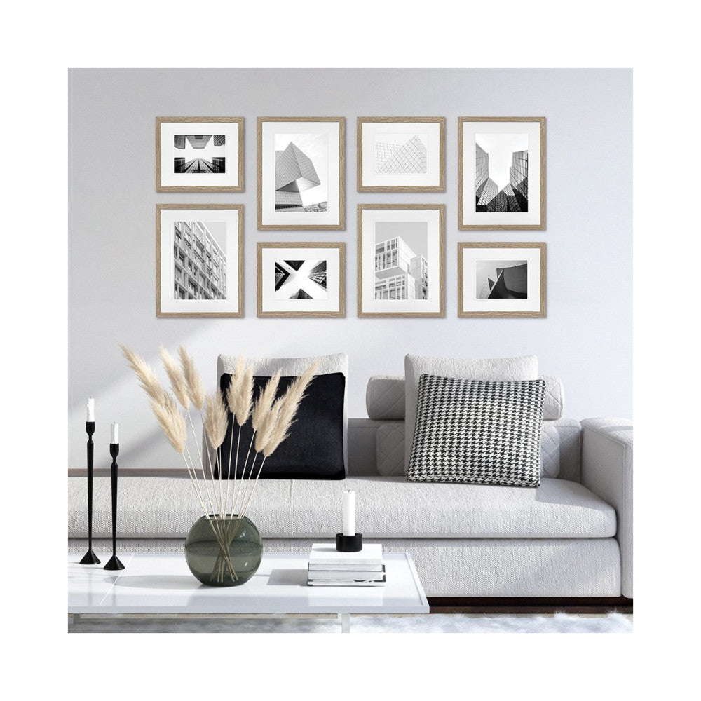 Eight framed black and white architectural photographs displayed on a light gray wall above a modern gray sofa with decorative pillows and accessories.
