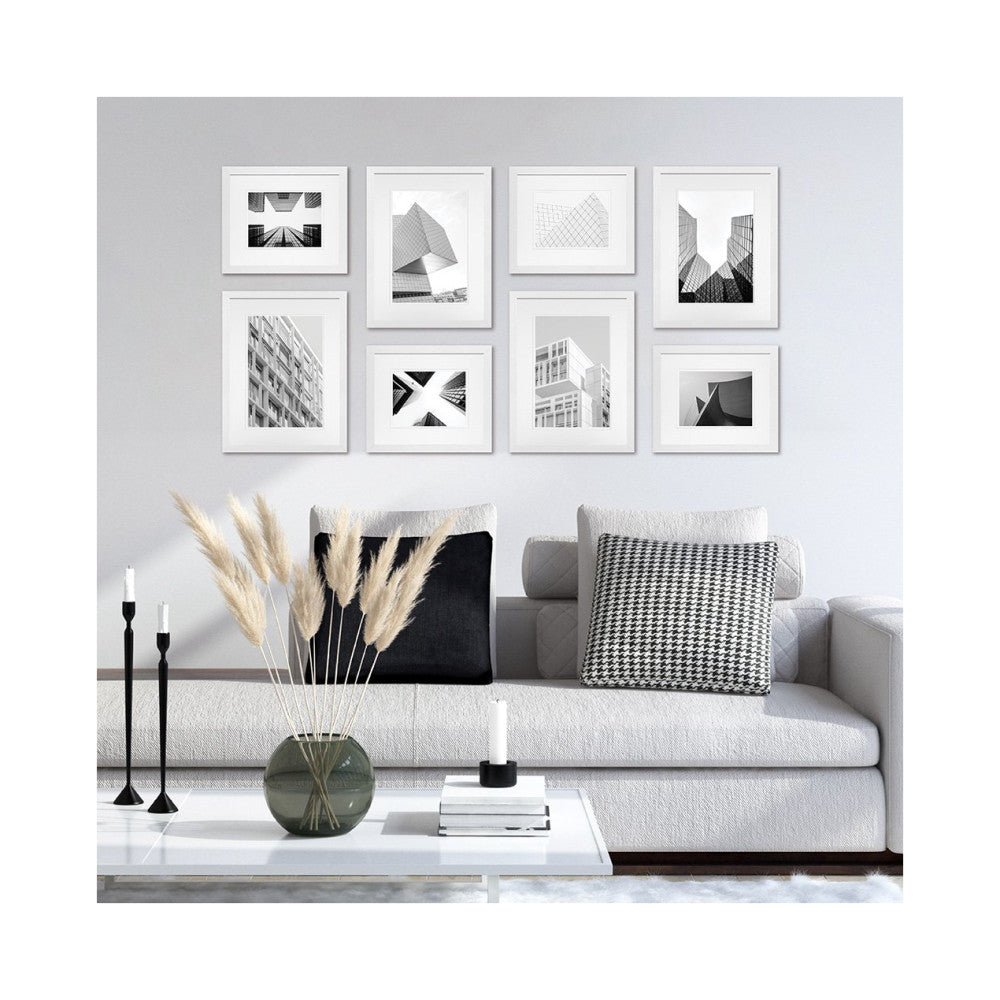 Eight white-framed black and white architectural photographs arranged on a light wall above a modern gray sofa with decorative pillows and accessories.