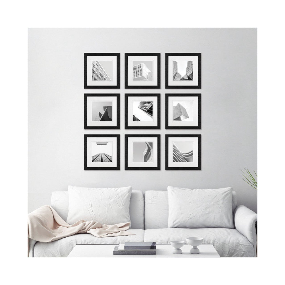 Nine black-framed architectural photographs arranged in a 3x3 grid on a light gray wall above a white sofa with pillows.